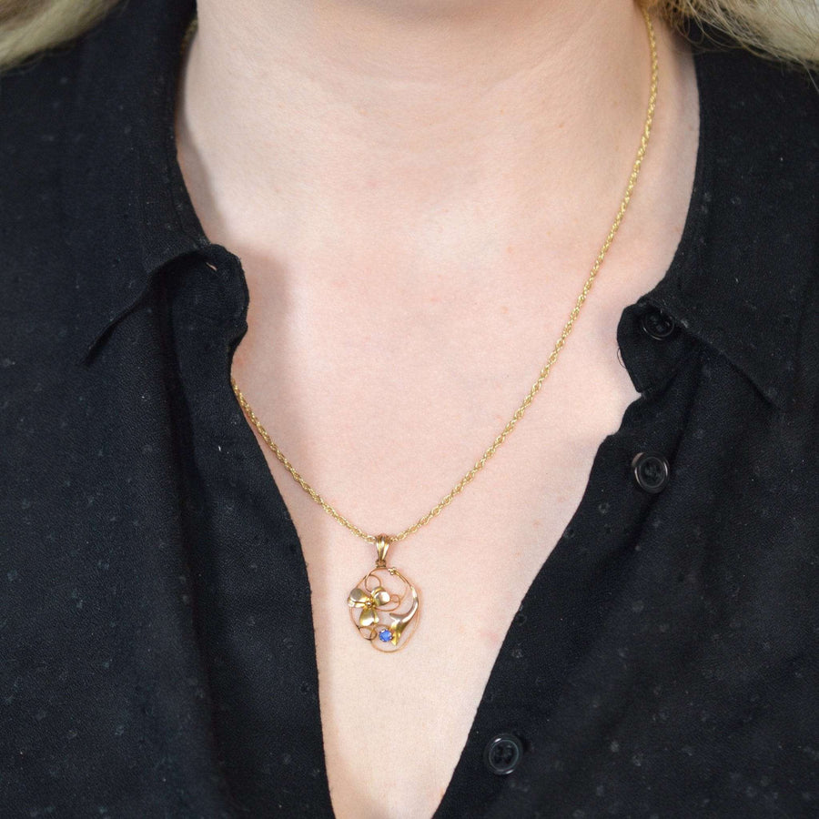 Woman wearing an Art Nouveau 9ct gold floral pendant with a sapphire, showcasing a delicate flower design.