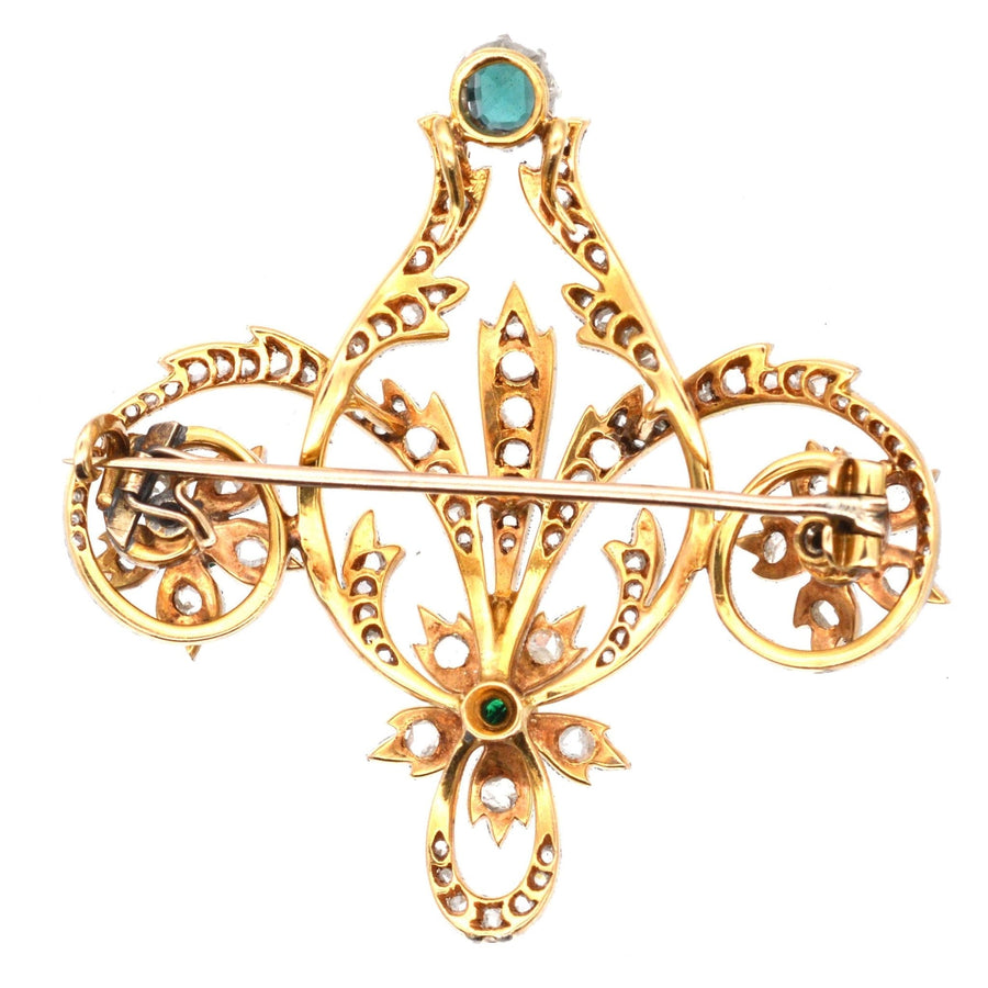 Edwardian gold brooch with emerald and rose diamonds, featuring intricate scroll and floral design.