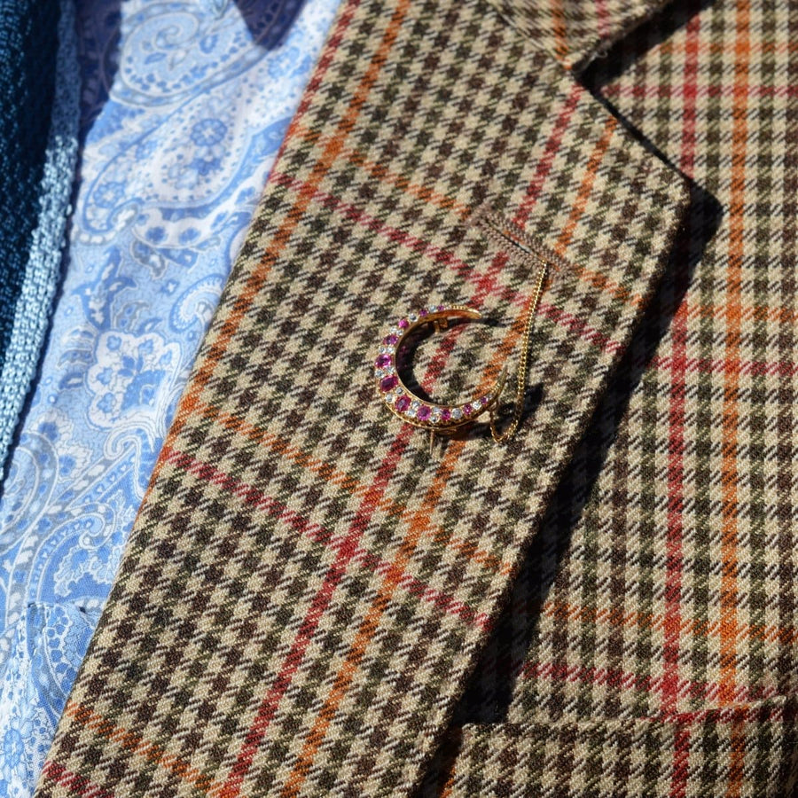 Edwardian 18ct gold crescent moon brooch with ruby and diamond on a patterned blazer lapel.