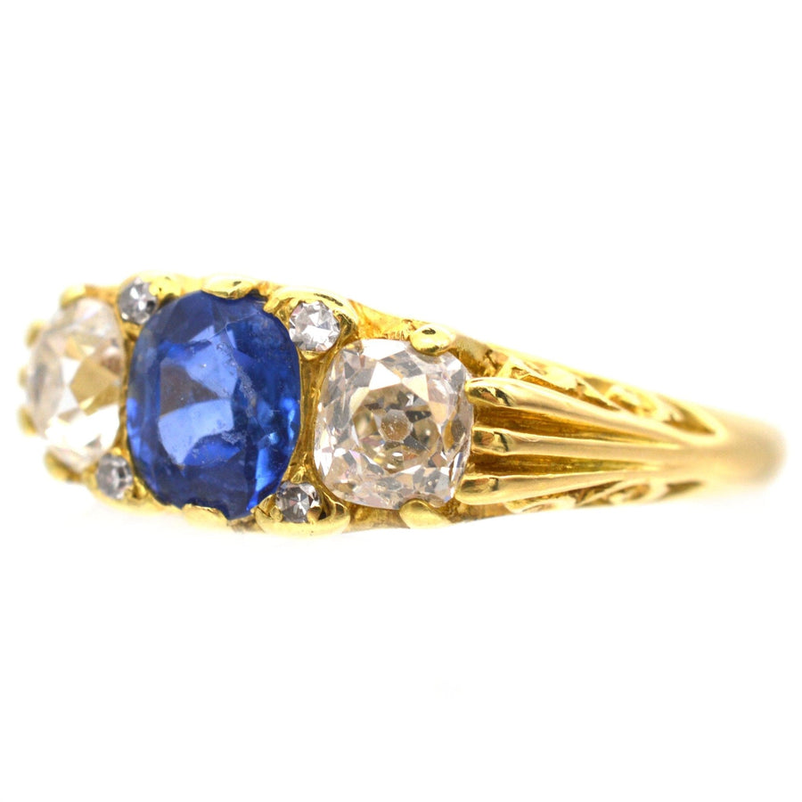 Victorian-style 18ct gold three stone sapphire and diamond ring with carved detailing and elegant blue sapphire centerpiece.