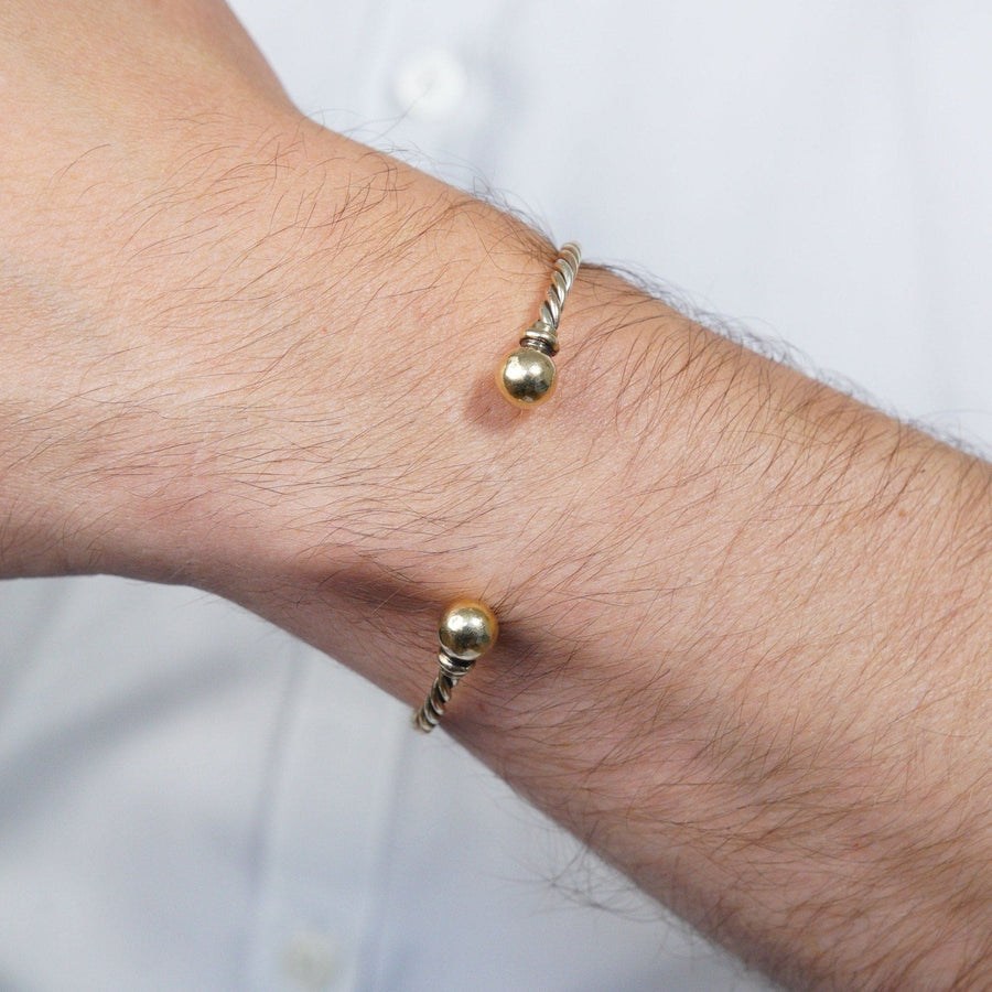 Vintage 9ct gold twisted three color gold open bangle worn on wrist, showcasing elegant design with gold spheres.