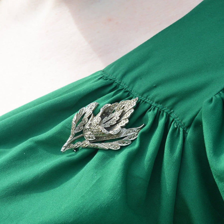 20 世纪 40 年代绿色礼服上的铬和黑云母花朵胸针，展现了复杂的设计和经典复古的优雅。