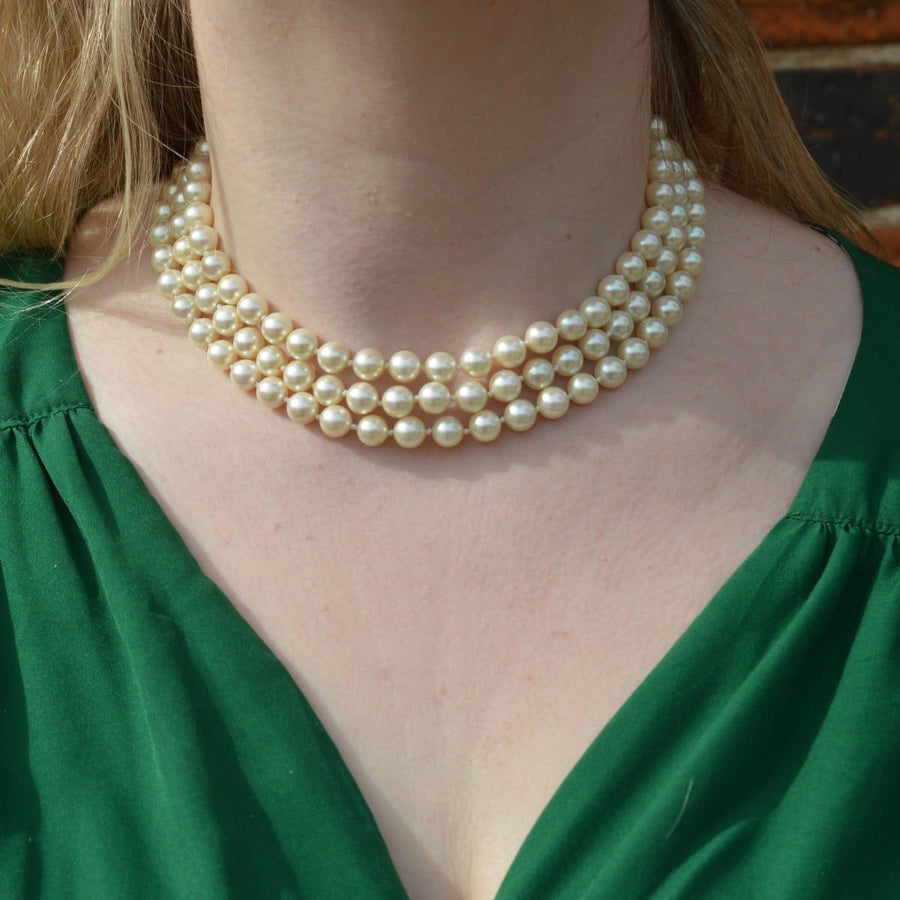 Three-strand pearl necklace elegantly worn, enhancing a green blouse with classic style and sophistication.
