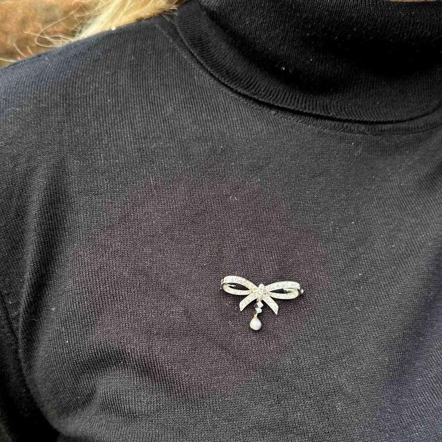 Early 20th century 14ct white gold diamond and grey pearl bow brooch worn on a black turtleneck.