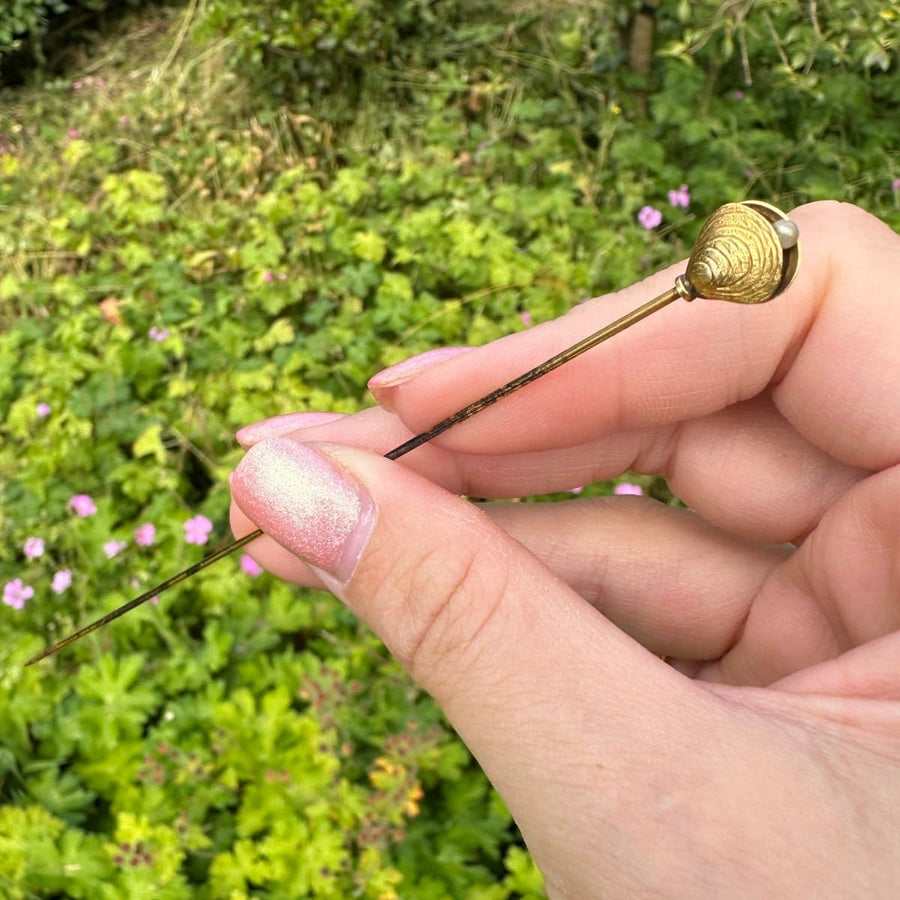 Edwardian 9ct gold oyster shell and pearl hat pin held in hand, showcasing intricate design in natural setting.