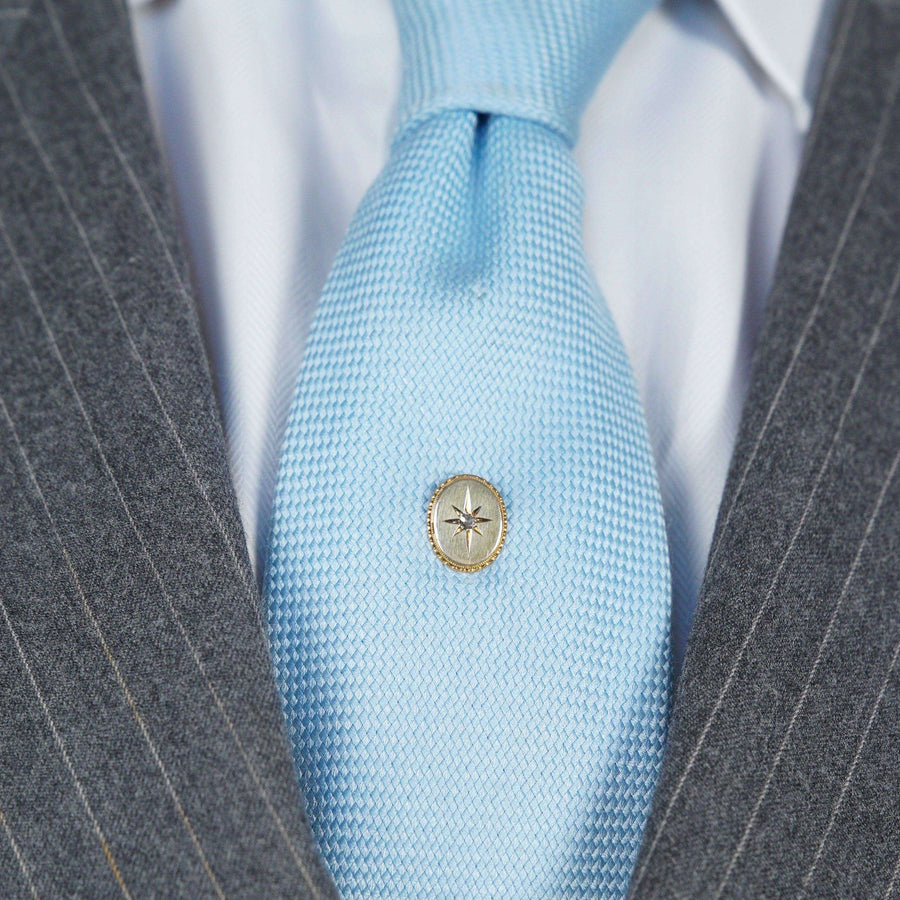Gold star tie pin with rose cut diamond on blue tie, enhancing classic formal attire.