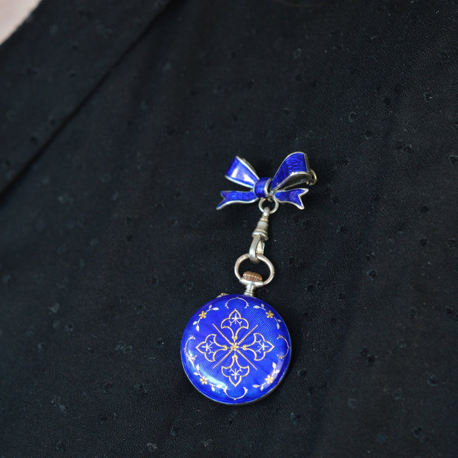 Edwardian silver pocket watch with royal blue guilloché enamel and bow, displayed against a black background.