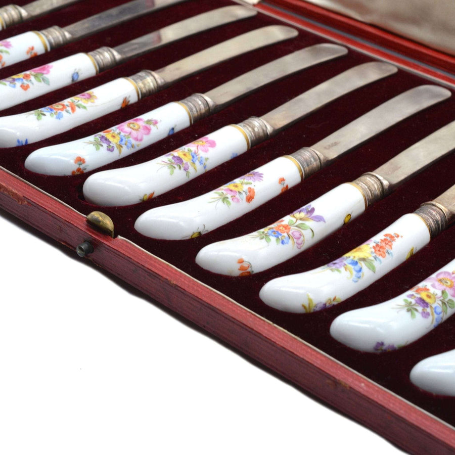 一套 12 把 19 世纪晚期托马斯-古德银刀，配有彩绘迈森瓷手柄，装在红色皮盒中。